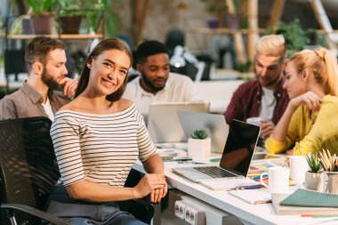 Kadın iç mimar kameraya gülümsüyor, ortak çalışma alanında çalışıyor.
