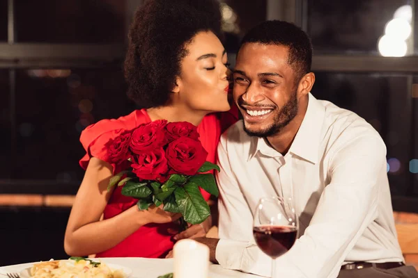 Dziewczyna całuje chłopaka po otrzymaniu róż podczas randki w restauracji — Zdjęcie stockowe