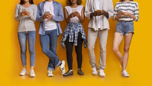 Cortado de amigos multiétnicos uisng smartphones sobre fundo amarelo — Fotografia de Stock