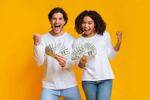 Γοητευμένο διαφυλετικό ζευγάρι που κρατάει πολλά δολάρια μετρητά, γιορτάζοντας την επιτυχία μαζί. — Φωτογραφία Αρχείου