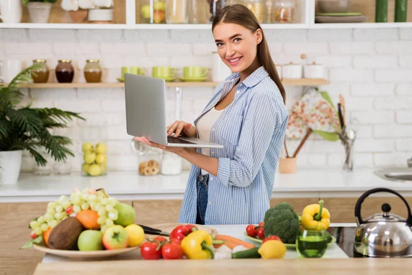 Receptsökning. Ung kvinna som använder laptop i köket — Stockfoto