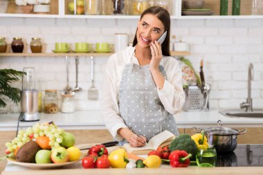 Woman talking on cellphone and writing new recipes clipart