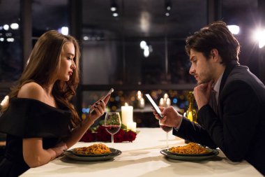 Genç adam ve kadın cep telefonlarıyla meşgul.