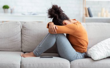 Depresyonda olan kadın, elleri içine gömülü, koltukta oturuyor.