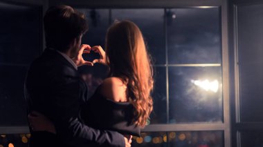 Mutlu adam ve kadın elleriyle kalp yapıyor, arkadan bakıyor.