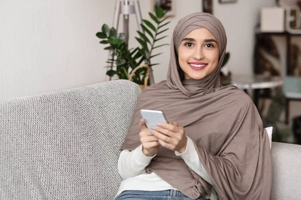Potret gadis arab yang tersenyum dengan menggunakan headscarf menggunakan smartphone di rumah — Stok Foto