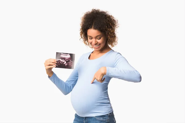 Feliz mujer embarazada mostrando ecografías y señalando el vientre —  Fotos de Stock