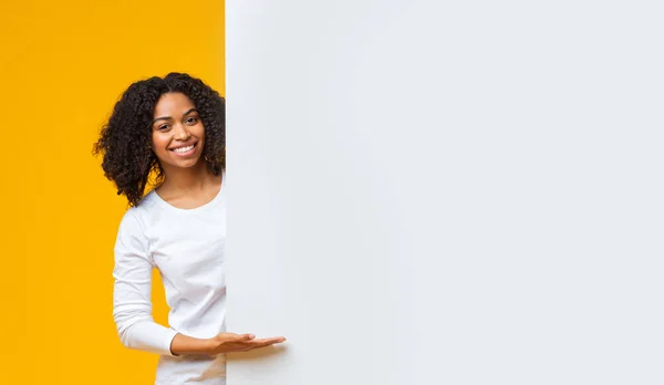 Glimlachend Afro meisje wijzend naar witte reclamebord voor uw tekst — Stockfoto