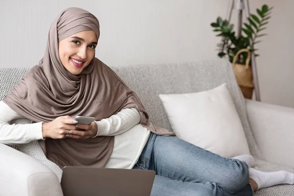 Vidám muszlim lány hidzsáb időt tölt okostelefonnal otthon — Stock Fotó