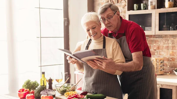 Senior pár čtení recepty v interiéru kuchyně, panorama — Stock fotografie