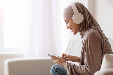 Müslüman kız evde kulaklıkla müzik dinlemek için akıllı telefon kullanıyor.
