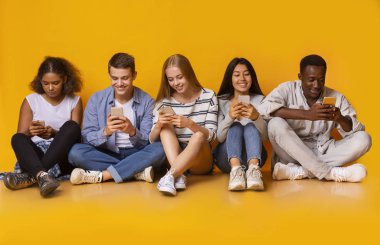 Gençler yerde oturup akıllı telefonlarıyla mesajlaşıyorlar.