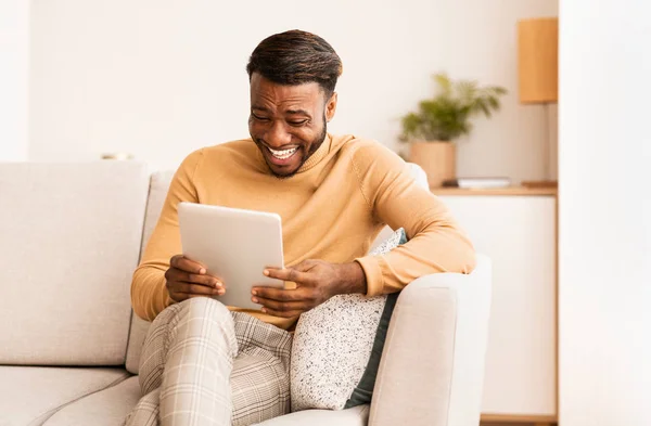 Afrikanisch-amerikanischer Mann sitzt lachend mit Tablet auf Sofa — Stockfoto