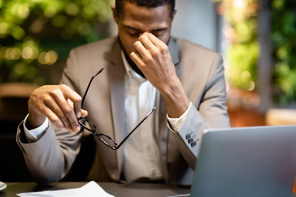 Exhausted afro manager massaging nose while using laptop — Stock Photo, Image