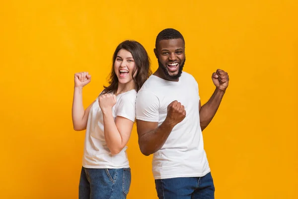 Glada multiracial par seger med upphöjda händer på gul bakgrund — Stockfoto