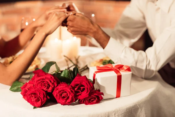 Casal segurando as mãos, presente dos namorados e rosas deitadas na mesa — Fotografia de Stock