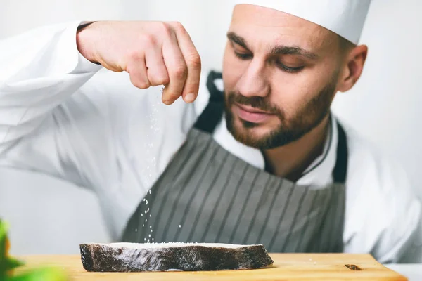 Mężczyzna kucharz sól ryba stek gotowanie w kuchnia wewnątrz — Zdjęcie stockowe