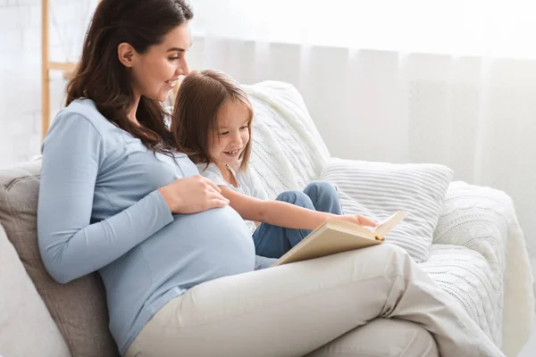 Gadis kecil dan ibu hamil menikmati buku bersama — Stok Foto