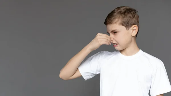 Disgusted teenager closing his nose, grey background — Stock Photo, Image