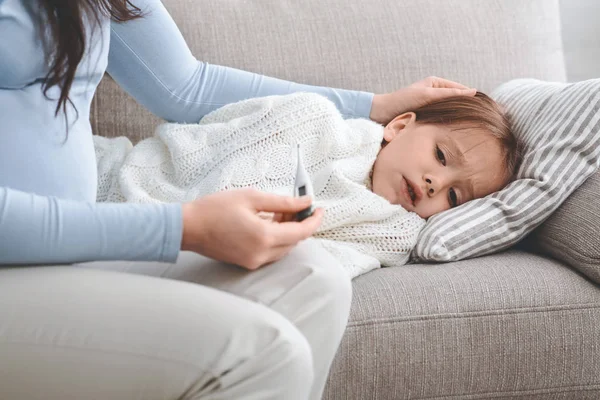 Pregnant mother checking her sick daughters temperature with thermometer — 스톡 사진