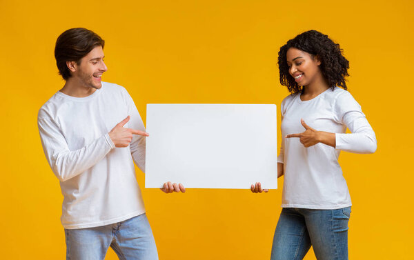 oyful interracial couple holding and pointing at blank advertisement placard