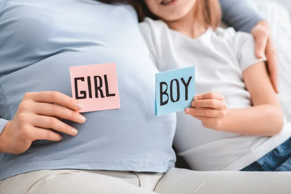 Mujer embarazada sosteniendo tarjetas rosas y azules al lado del vientre —  Fotos de Stock