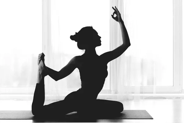 Silhouette einer fitten Frau, die Yoga drinnen über Fenster praktiziert — Stockfoto