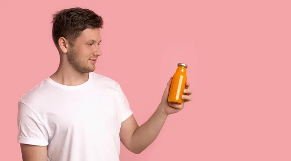 ชายหนุ่มที่น่าสนใจมองขวดที่มีเครื่องดื่มดีท็อกซ์สีส้ม — ภาพถ่ายสต็อก