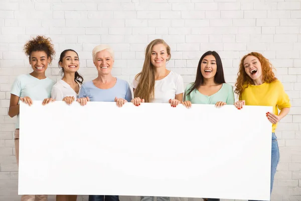 Mujeres sosteniendo cartel blanco vacío de pie sobre la pared blanca, burla — Foto de Stock