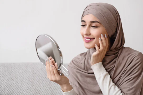 Wanita muslim cantik memegang cermin dan menyentuh kulitnya yang sempurna — Stok Foto