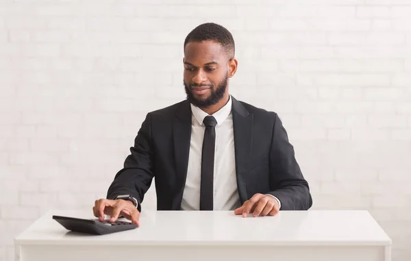 Zwarte ondernemer zittend aan het bureau en met behulp van rekenmachine — Stockfoto