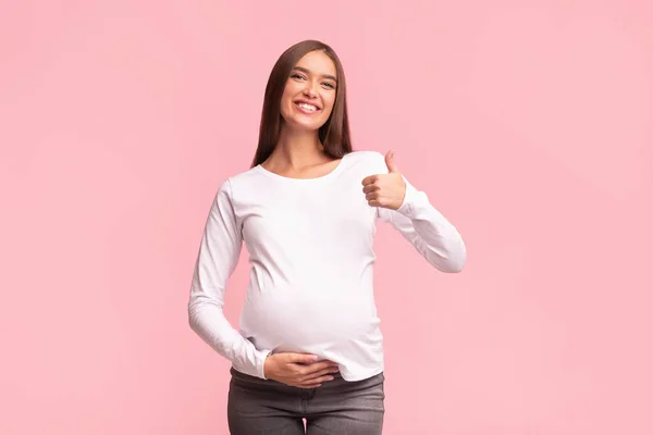 朗らかな妊娠中の女性はピンクの背景の上に親指を立てる — ストック写真