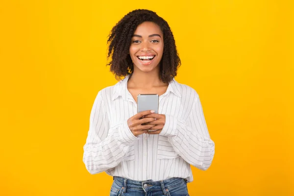 Sonriendo afro chica usando el teléfono celular mirando a la cámara — Foto de Stock