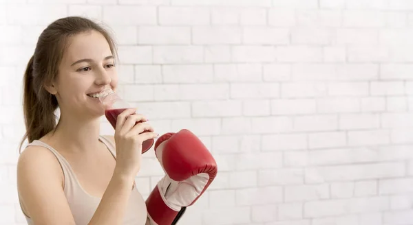 Mulher em luva de boxe bebendo smoothie desintoxicação vermelha sobre parede de tijolos brancos — Fotografia de Stock