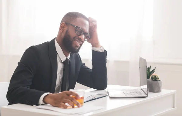 Hombre de negocios negro cansado bebiendo alcohol en el lugar de trabajo —  Fotos de Stock