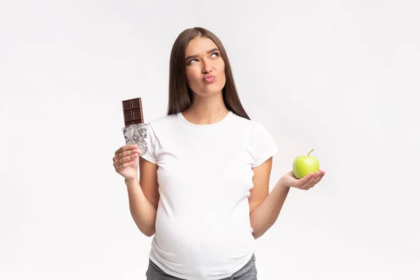 妊娠中の女性がスタジオでチョコレートとアップルの間で選択パズル — ストック写真
