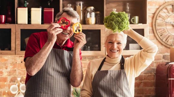 Idosos alegres brincando com legumes frescos na cozinha — Fotografia de Stock