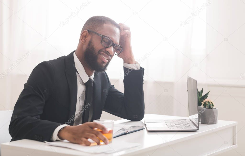 Tired black businessman drinking alcohol at workplace