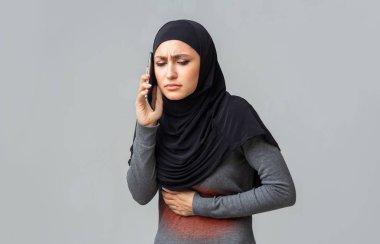 Karın ağrısı çeken Müslüman bir kadın cep telefonuyla doktorla konuşuyor.
