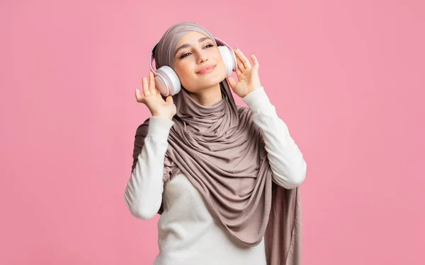 Joyful arabic girl in hijab listening favorite music with wireless headphone — Stok Foto