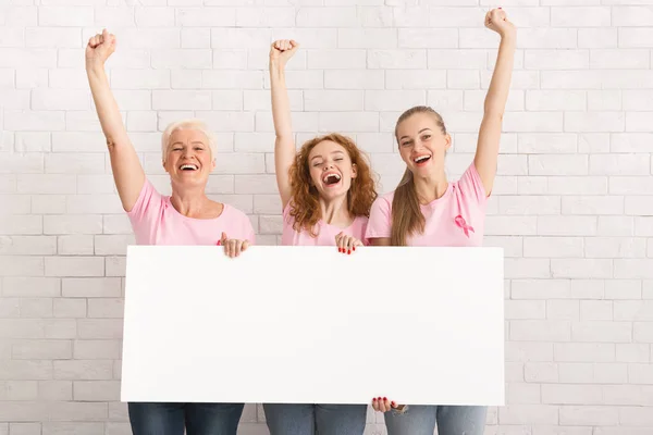 Tres mujeres en camisetas rosadas sosteniendo cartel sobre pared blanca — Foto de Stock