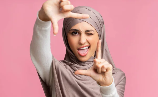 Playful muslim woman in headscarf framing face with fingers and winking — Stock Photo, Image