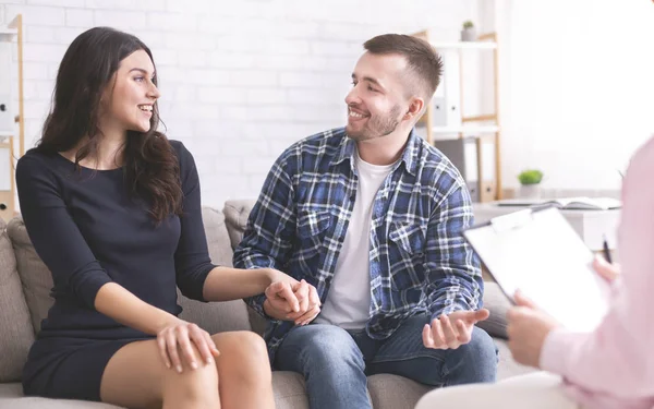 Cheerful millennial spouses smiling to each other at consultation