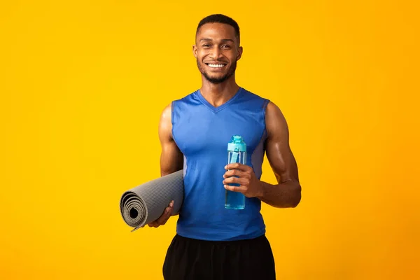 Afro αθλητής κρατώντας μπουκάλι νερό και ματ — Φωτογραφία Αρχείου