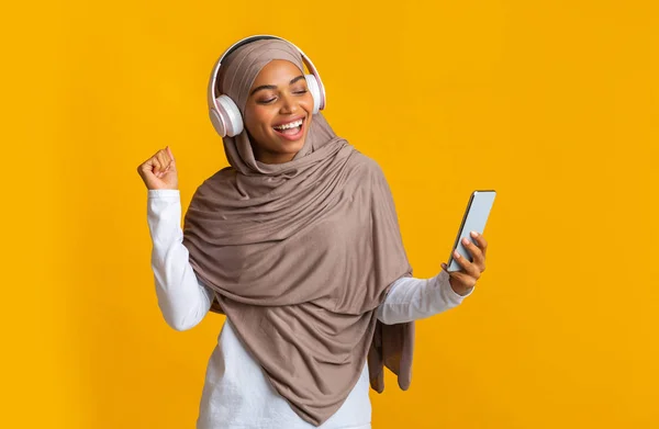 Joyeuse fille musulmane noire dans un casque sans fil écoutant de la musique sur smartphone — Photo