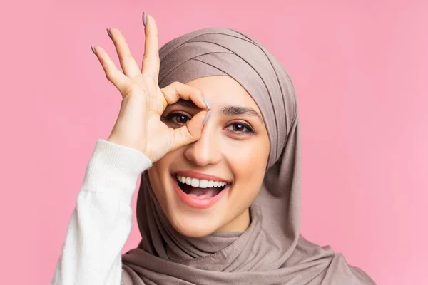 Fröhliche muslimische Frau im Hijab zeigt ok Geste und schaut durch die Finger — Stockfoto