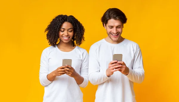 Sorrindo casal interracial ocupado com seus smartphones, tendo vício gadget — Fotografia de Stock