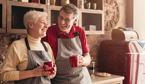 Happy senior couple drinking coffee at kitchen, panorama