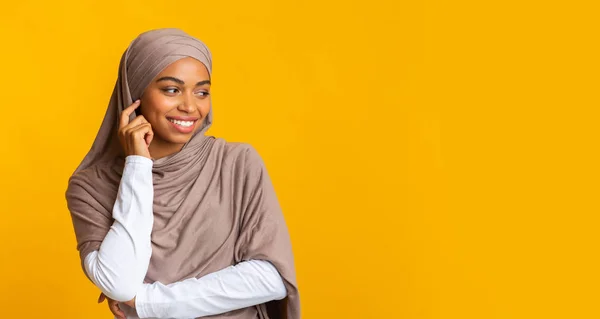 Interested black muslim girl looking away at copy space on yellow background — Stock Photo, Image