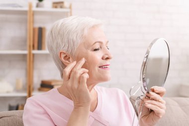 Kıdemli bayan kırışıklıkların etrafına yaşlanma önleyici krem sürüyor.